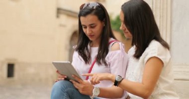 Tablet tutarak ve bakarak iki sevimli genç kadın. Mutlu ve heyecanlı hissediyorum. Açık havada.