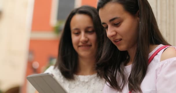 Hermosas chicas sentadas al aire libre y mirando el dispositivo de pantalla táctil. Están felizmente charlando. Al aire libre . — Vídeos de Stock