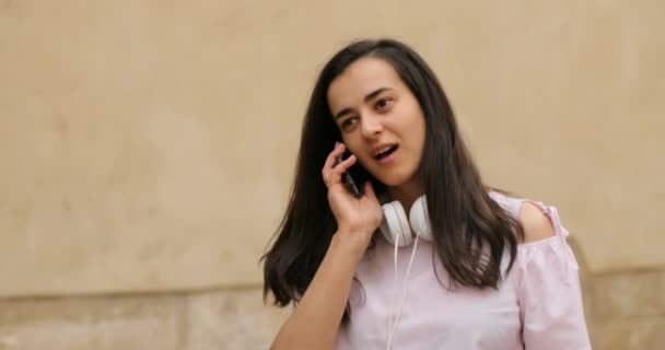 Young brunette female is talking on the phone. The girl is smiling and looking happy. Outdoors. — Stock Video