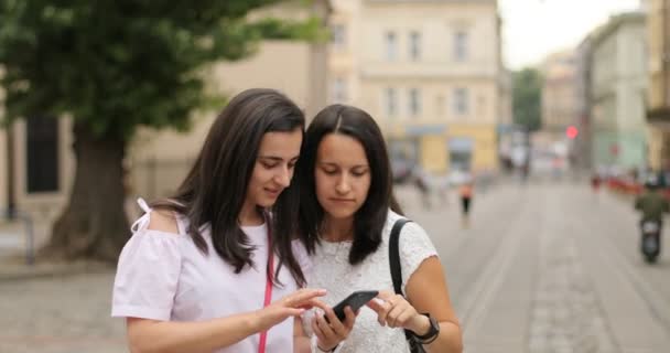 Dos chicas guapas usando el celular. Ambas hermanas felices y emocionadas. Al aire libre . — Vídeos de Stock