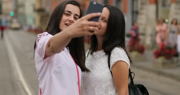 Chicas atractivas se están tomando selfies con su celular. Las morenas sonríen y se ven muy felices. Al aire libre . — Vídeos de Stock