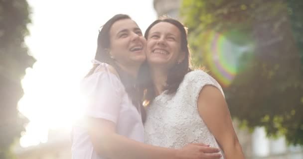 Dos hermosas hermanas caucásicas sonriendo y abrazándose en el parque de la ciudad. Al aire libre . — Vídeos de Stock