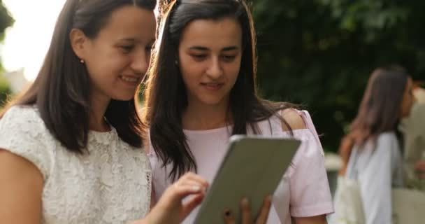 Twee gelukkige meisjes controleren van de tablet. Vriendinnen zijn buiten. — Stockvideo