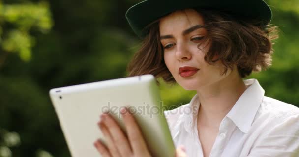 Молодая студентка с планшетным компьютером в парке Женщина печатает что-то на сенсорной панели, в то время как сидит против удивительного ландшафта — стоковое видео