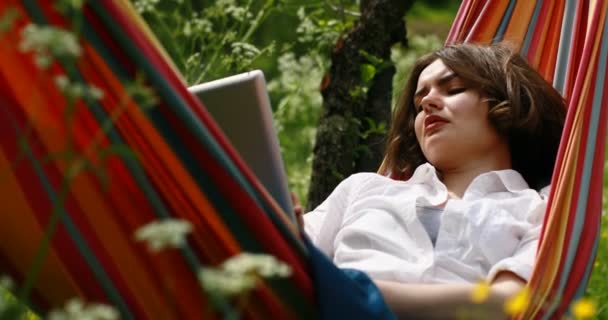 Jeune femme couchée sur un hamac dans la forêt d'été en utilisant une tablette numérique pc . — Video