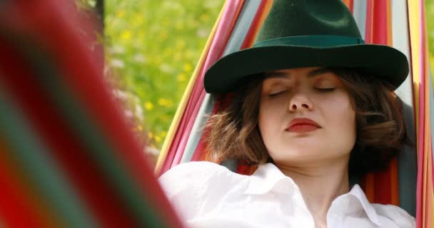 Fiatal nő kalapban fekve egy függőágyban próbál aludni nyári erdőben — Stock videók