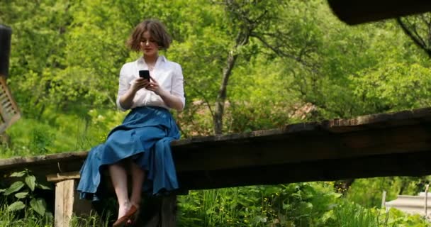 Caucasiano jovem mulher sorridente no parque mensagens de texto com seu smartphone, ela é redes sociais e bate-papo — Vídeo de Stock