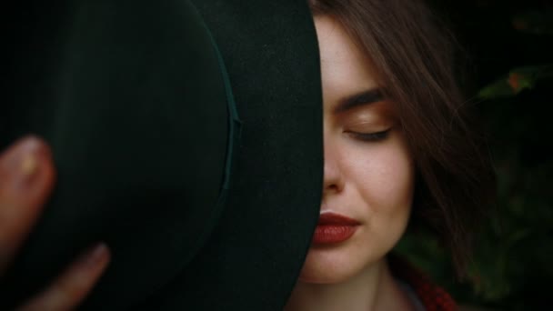 Κοντινό πλάνο με πορτρέτο του μια νεαρή όμορφη μοντέρνα γυναίκα που φοράει κομψό καπέλο. Τα κρυμμένα μάτια με καπέλο. Ομορφιά μελαχρινή βλέπουν φωτογραφική μηχανή — Αρχείο Βίντεο