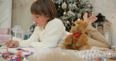 Küçük kız oyuncak ayı ile dekore edilmiş Noel ağacının yanında yalan ve Noel Baba'ya mektup yazma. Noel ağacı backgroung. Tatil ve yeni yıl.
