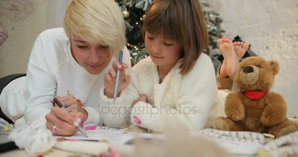 X-mas party celebration, childhood. Portrait of Mother and daughter is lying near decorated christmas tree and writing christmas letter to Santa Claus — Stock Video