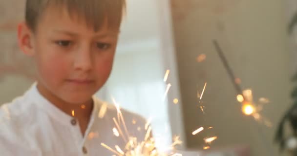 Close-up portrait of child boy holds lighted fireworks in the glitter background with bright golden Christmas lights. Meeting the new year. Christmas party — Stock Video