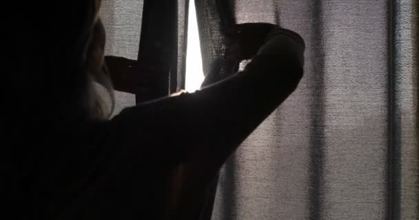 Ung flicka öppnar gardinerna på morgonen på en solig dag. Bakifrån sköt. — Stockvideo