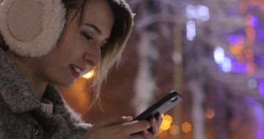 Geceleri, gülümseyen ve manifatura üstünde hareket eden telefon smartphone cep telefonu ile şehir içinde app kullanan kadın. Güzel çok kültürlü genç casual kadın üstünde hareket eden telefon.