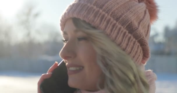 Primer plano de la joven hablando por teléfono, cruzando la calle de la ciudad de invierno, Navidad de nieve. Mujer vistiendo un abrigo de invierno y rosa bufanda y sombrero — Vídeos de Stock