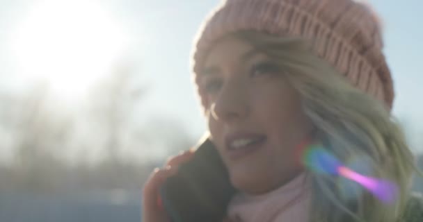 Крупный план, где молодая девушка разговаривает по телефону, переходит улицу Зимнего города, снежное Рождество. Женщина в зимнем пальто и розовом шарфе и шляпе — стоковое видео