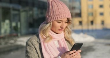 Çağrı yanıtlanıyor, akıllı telefonda konuşurken mutlu kız. Kadın giyen bir kış ceket ve pembe atkı ve şapka. Modern bina arka plan