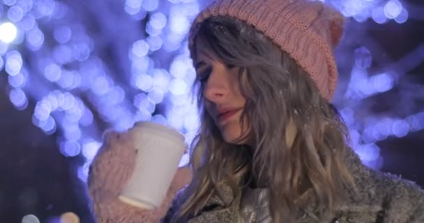 Porträtt av leende kvinna i rosa varma kläder dricka kaffe att ta bort över snöiga natt staden bakgrund. Lycka, vintern semester, jul, drycker — Stockvideo