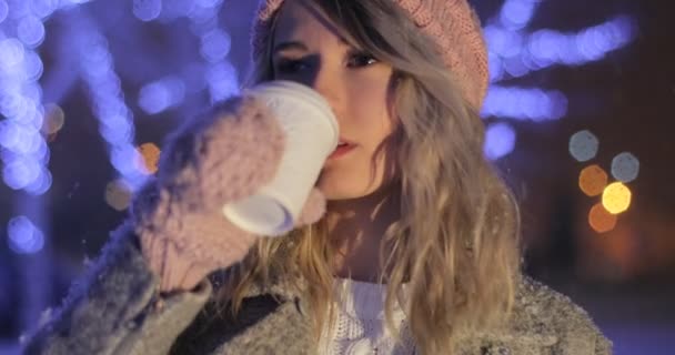 Mujer sonriente con ropa de abrigo rosa bebiendo café para llevar sobre fondo nevado de la ciudad. Felicidad, vacaciones de invierno, Navidad, bebidas — Vídeos de Stock