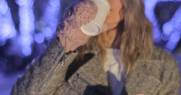 Retrato de mulher sorridente em roupas quentes cor-de-rosa bebendo café para levar embora sobre fundo da cidade noite nevada. Felicidade, férias de inverno, Natal, bebidas — Vídeo de Stock