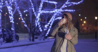 Karlı gece şehir arka plan üzerinde götürmeye gülümseyen kadın kahve içme pembe sıcak giysiler içinde. Mutluluk, kış tatil günleri, Noel, içecekler