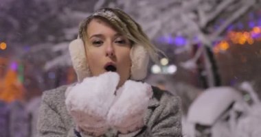 Gece kış City, kameraya arayan kadın kar üfleme güzel mutlu kız portresi. Şık klasik kış giyim Bayan giyim örme. . Açık havada. Uçan Kar taneleri,