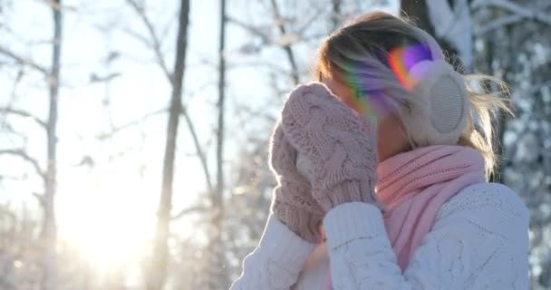 Jovem bebe chá quente ou café da xícara no acolhedor parque nevado no inverno. Menina bonita desfrutando de inverno ao ar livre com uma caneca de bebida quente. Dia ensolarado, menina olhando para a câmera — Vídeo de Stock