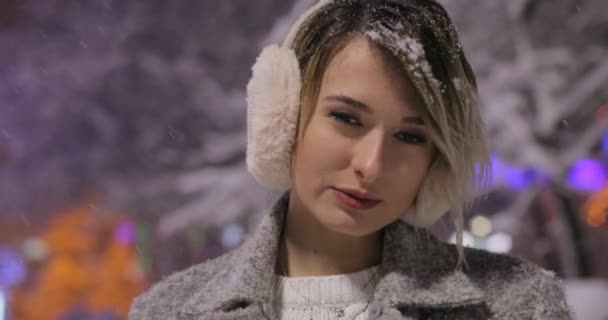 Αστική συναισθηματική πορτρέτο του όμορφη κοπέλα στην πόλη Χειμερινή νύχτα, γυναίκα βλέπουν φωτογραφική μηχανή. Κυρία φορούσε κομψό κλασικό χειμώνα πλεκτά ρούχα. Που φέρουν νιφάδες χιονιού, — Αρχείο Βίντεο