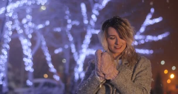 Retrato de una joven mujer con orejeras con la cabeza inclinada, tratando de calentarse en la ciudad de invierno por la noche. Concepto de invierno. Navidad, concepto de vacaciones de invierno. Nieve . — Vídeos de Stock