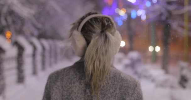 Retrato de uma jovem mulher sorrindo usando abafadores de ouvido, na cidade de inverno da noite. Conceito de inverno. Natal, conceito de férias de inverno. Queda de neve . — Vídeo de Stock