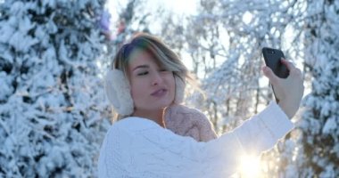Bir selfie smartphone ile açık havada kışın alarak beautifuln genç kız ile kulak muffs, portresi. Noel, kış tatil kavramı. Kadın sallanan el kamera için
