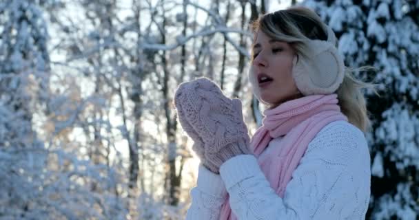 イヤーマフ、凍るような冬の公園の持つ美しい幸せな女の子の肖像画。アウトドア。フライング雪、晴れた日。バックライト付き。カメラ、うれしそうな陽気な気分、感情に笑顔 — ストック動画