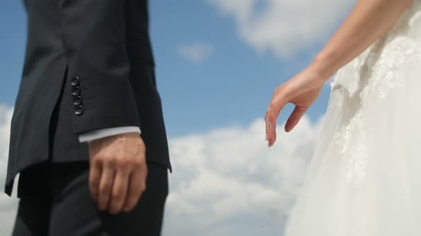 Újonnan házas esküvő házaspár tartja kezében a felhők háttér. A vőlegény a menyasszonyt veszi a kezét — Stock videók