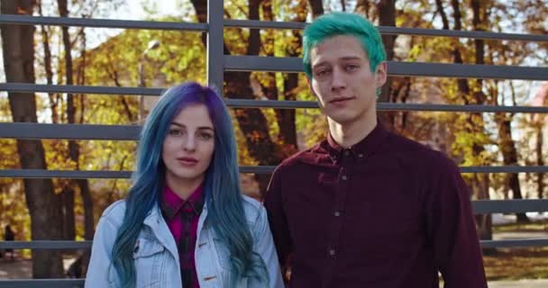 Unga kaukasiska hipster par kär i blått hår ler rakt mot kameran i parken på hösten. Utomhus. Porträtt skjuten. — Stockvideo