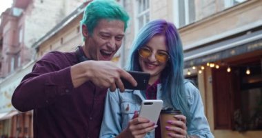 Genç beyaz erkek ve kız, mavi saçlı hippiler, akıllı telefondan komik bir şey izlerken gülüyorlar..