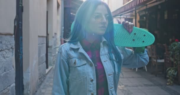 Kamera přiblížení na mladé bělošské hipster stylu dívka s modrými vlasy a s skateboard procházky po ulici ve městě. Portrét. Zavřít. — Stock video