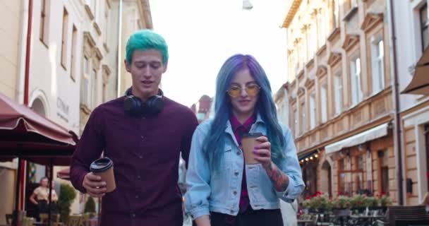 Fiatal kaukázusi divatos pár kék hajú, akik a város utcáin sétálnak, nevetnek és kávét isznak, miközben élvezik az együtt töltött időt.. — Stock videók