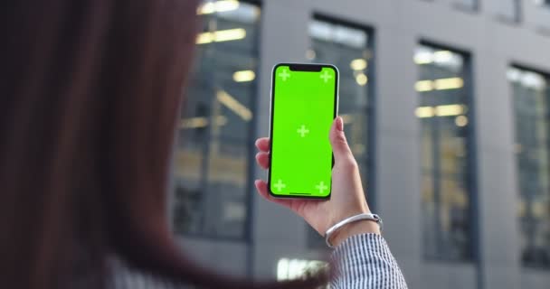 Widok przez ramię na białą brunetkę trzymającą smartfona z zielonym ekranem i śledzącą ruch. Na zewnątrz. Klucz chromowy. — Wideo stockowe