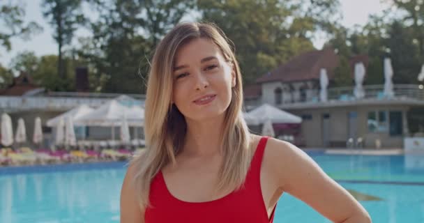 Ritratto della bella bionda caucasica con il costume da bagno rosso che sorride alla telecamera della piscina del resort. Da vicino. . — Video Stock