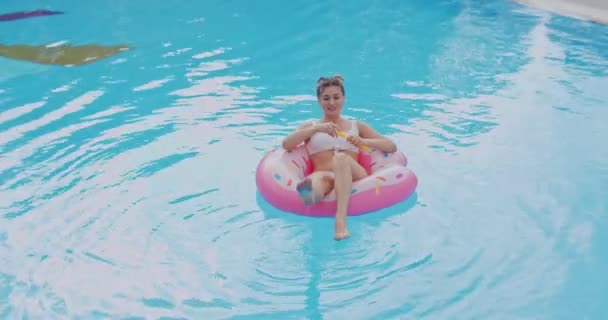 Junge kaukasische hübsche blonde Frau schwimmt auf dem rosafarbenen Schwimmer und pustet im Urlaub fröhlich Seifenblasen. — Stockvideo