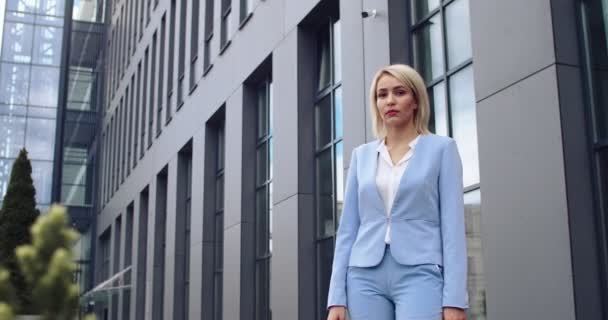 Kavkazská mladá krásná a stylová blondýnka v modrém kostýmu, stojící venku v obchodním centru a pózující na kameru s úsměvem. Portrétní snímek. — Stock video