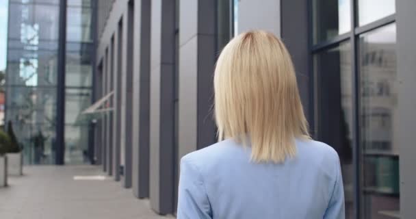 Vista posteriore sulla giovane donna bionda caucasica in stile business che cammina all'esterno del moderno edificio per uffici. Posteriore . — Video Stock