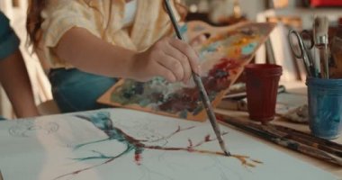 Genç ve güzel beyaz kadın ressamın, hoş sanat stüdyosundaki boyalarıyla bir ağaç boyamasına yakından bakın..