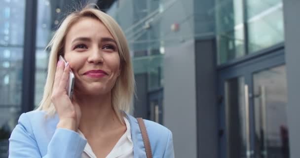 Närbild av den unga blonda kaukasiska charmiga och framgångsrika kvinna som går utomhus på gatan på morgonen och talar i telefon. — Stockvideo