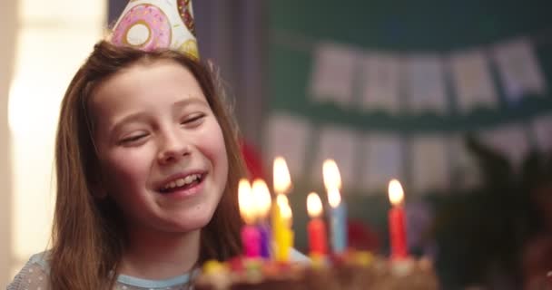 Primer plano de la niña linda caucásica en un cono celebrando su cumpleaños, soplando velas en el pastel y sonriendo. Retrato . — Vídeo de stock