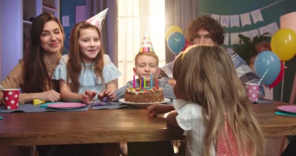 Cámara zoom en el pequeño chico lindo caucásico sentado en la mesa con su familia en la mesa con pastel de cumpleaños . — Vídeos de Stock