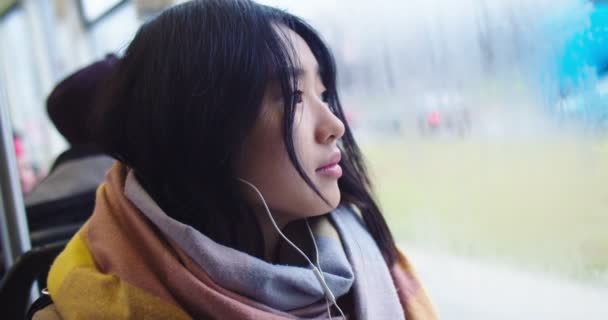 Retrato de la joven asiática hermosa chica en auriculares litening a la música y mirando a la ventana, luego girando a la cámara y sonriendo alegremente en el tranvía o autobús . — Vídeo de stock