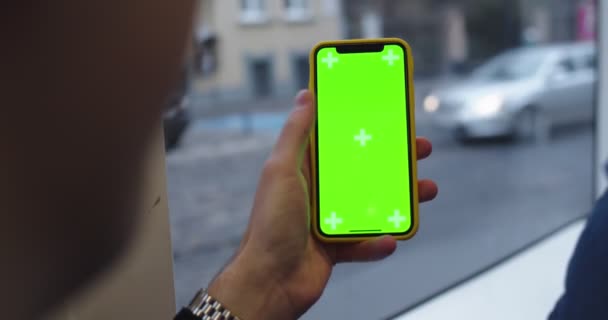 Viena, Austria - 25.11.2019: Close up of the male Caucasian hand holding vertical smartphone with chroma key screen and tracking motion while man sitting at the window in the moving tram or bus. — Stok video