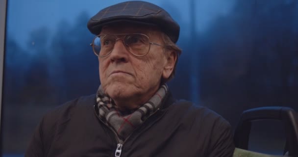 Primer plano del viejo hombre caucásico pensionista en las gafas y gorra sentado en el tranvía o en un autobús por la noche al volver a casa . — Vídeos de Stock