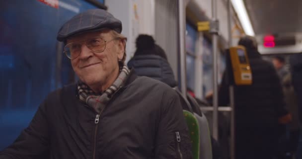 Old Caucasian man in the coat, glasses and hat smiling and talking with somebody while sitting at the window at the tram or bus in the evening. — Stock Video