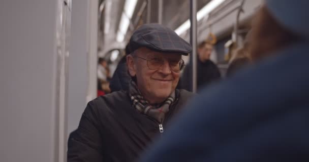 Homem velho caucasiano de óculos e chapéu sorrindo e falando com alguém enquanto volta para casa no bonde ou ônibus à noite . — Vídeo de Stock